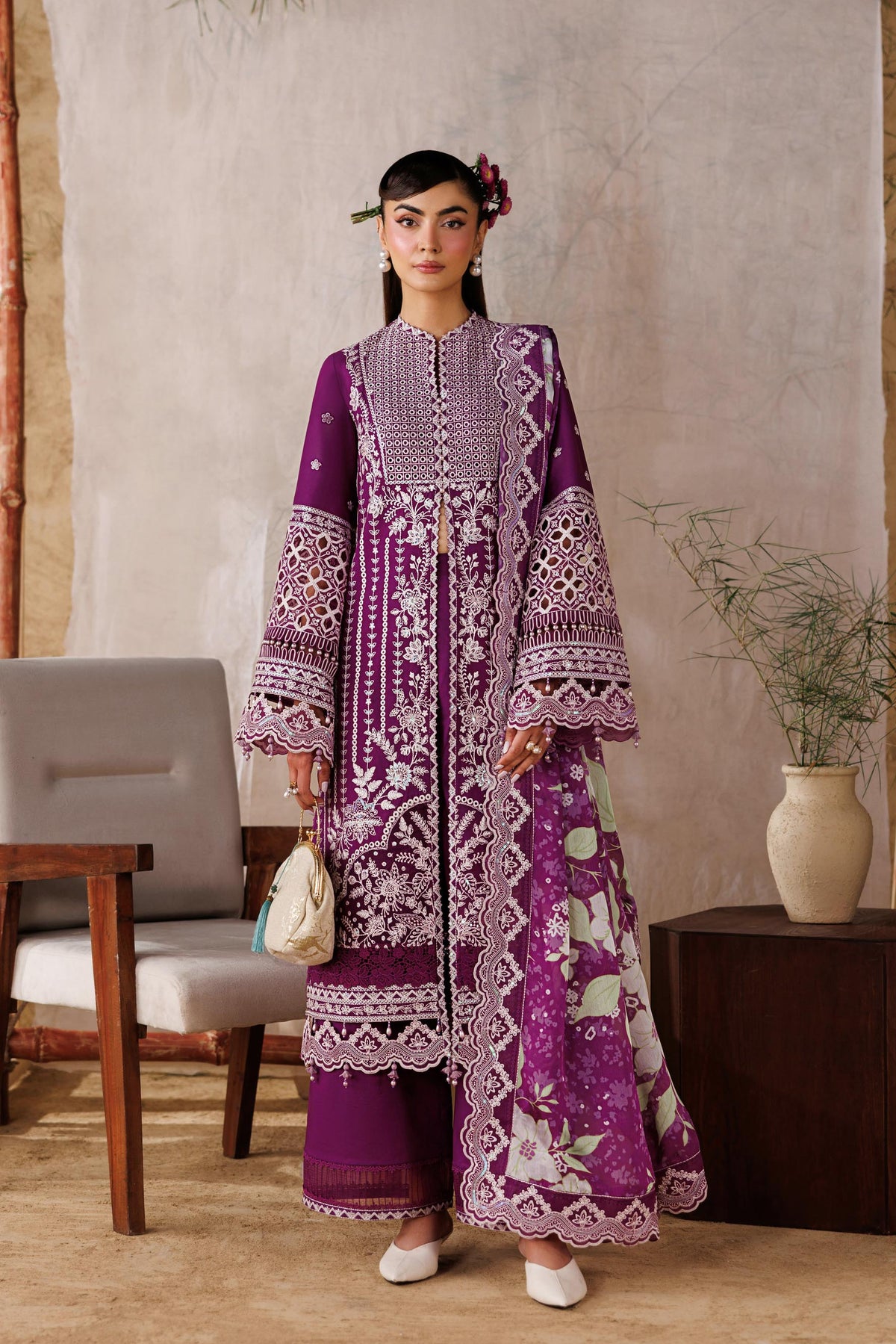 Woman in a purple embroidered outfit standing in front of a white curtain with a wooden frame.