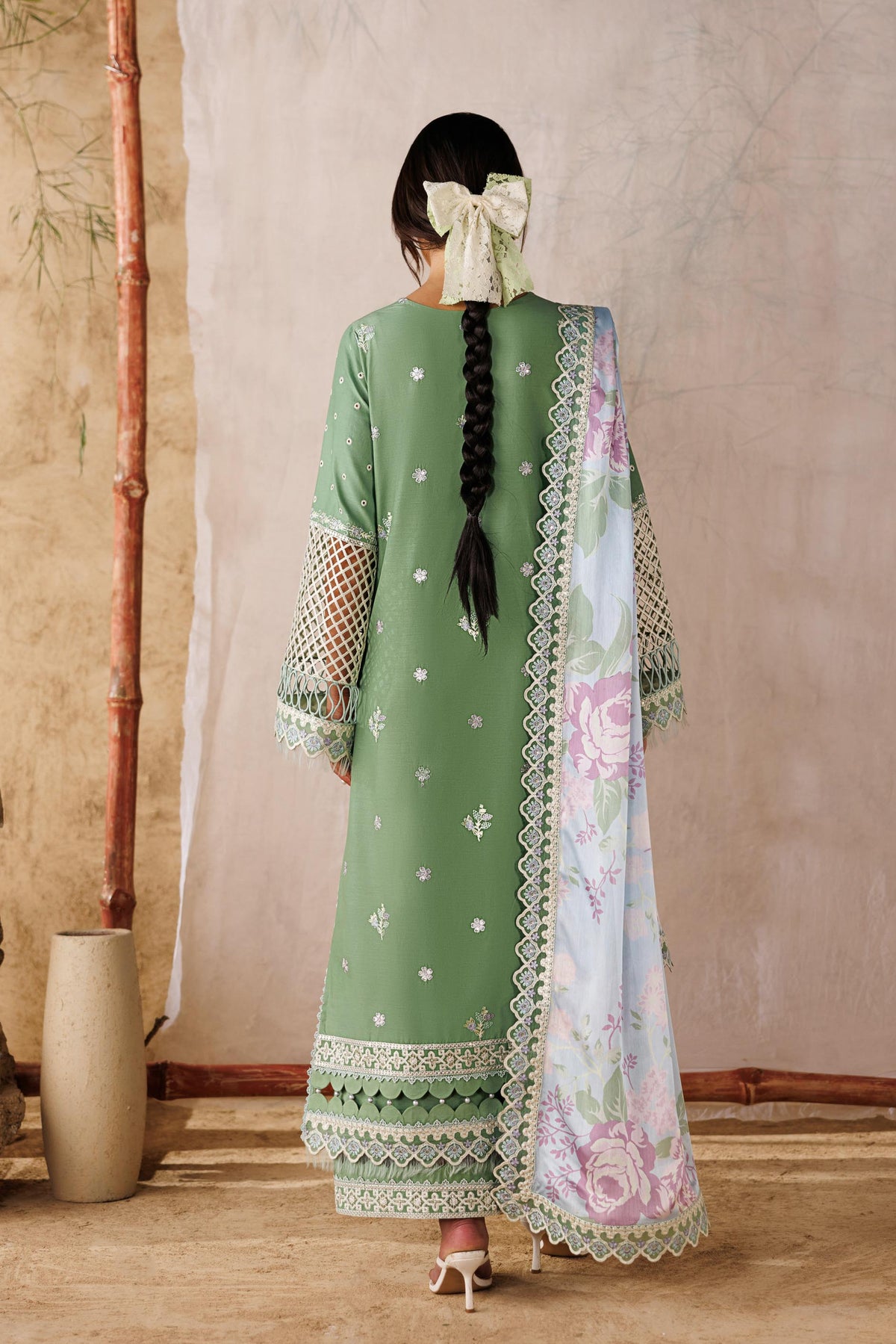 Woman in a green traditional outfit with a floral dupatta standing against a neutral wall.