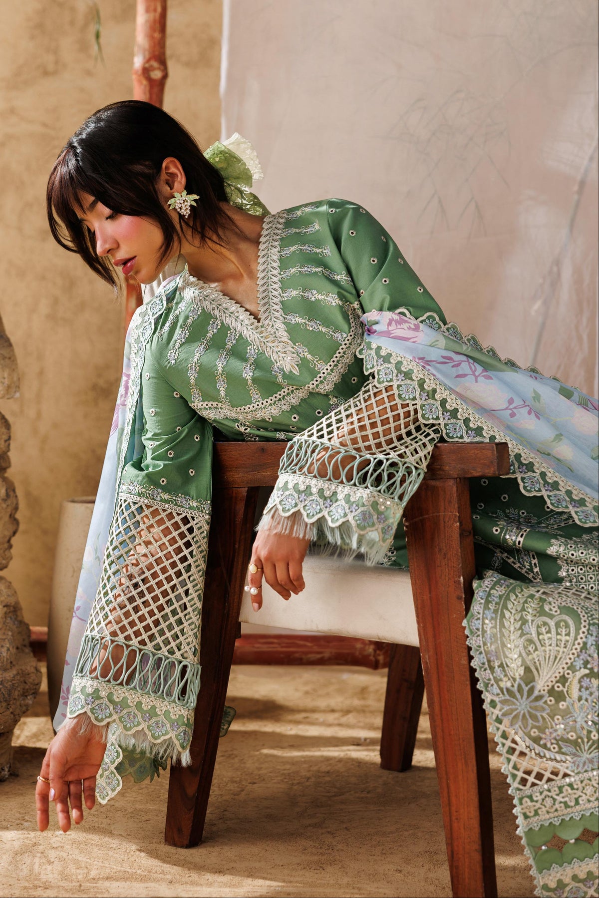 Woman in a green and white patterned dress sitting on a wooden chair.