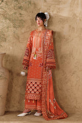 Woman in an orange embroidered outfit standing against a textured beige wall with decorative vases and plants.