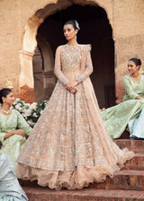 A woman wearing an elegant bridal gown with intricate embroidery and a flowing skirt, posing in a traditional setting.