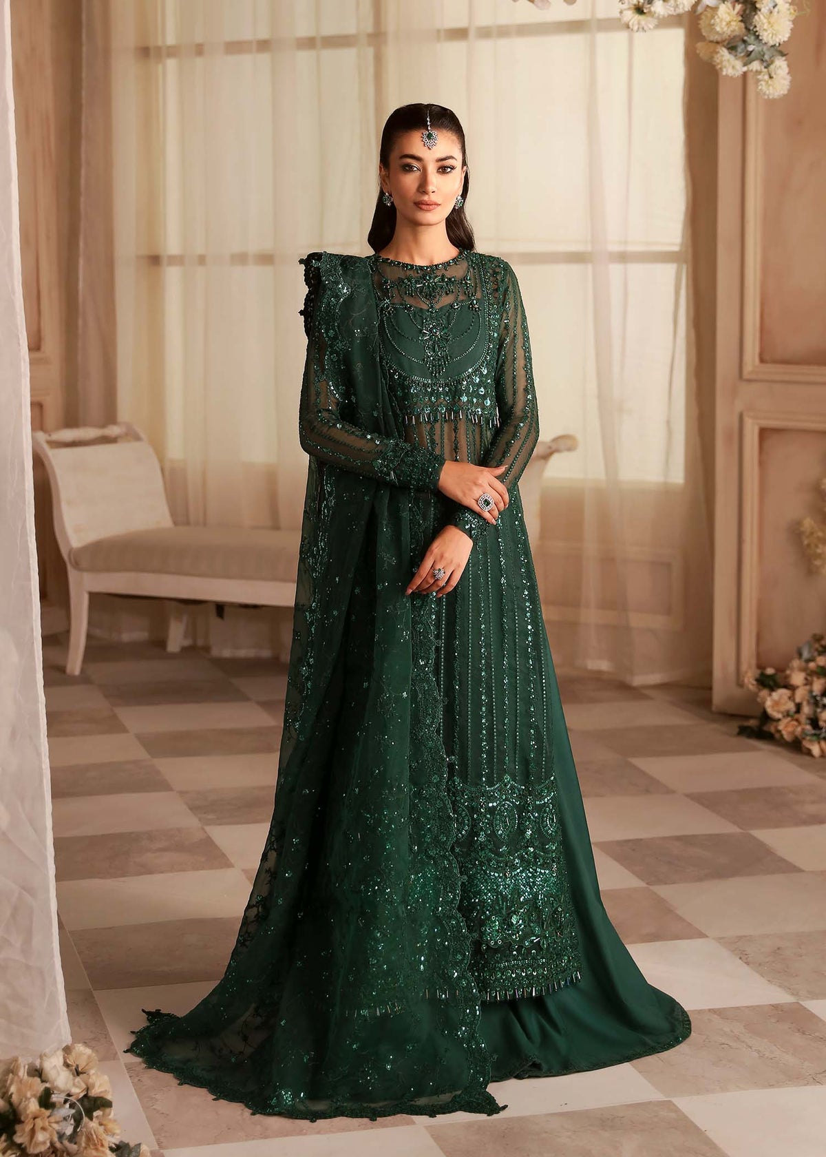 A woman wearing an emerald green, organza embroidered dress with sequins and beadwork, featuring long sleeves and a V-neckline.