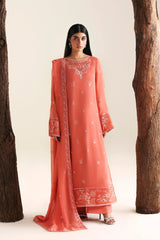 Woman wearing a coral pink traditional outfit with intricate patterns, standing between two large wooden logs on a white background.