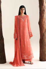 Woman wearing a coral pink traditional outfit with intricate patterns, standing between two large wooden logs on a white background.