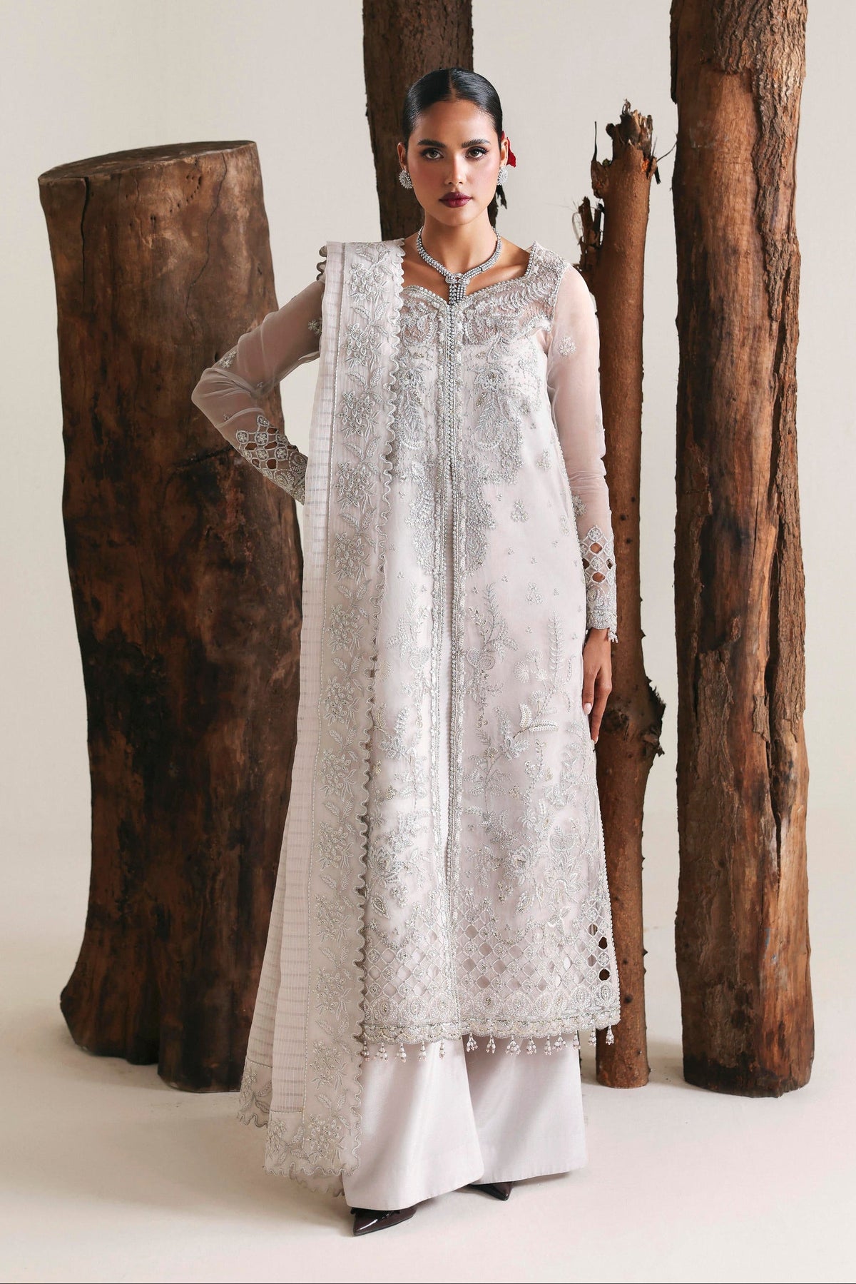 Woman in a white traditional outfit standing next to large wooden logs on a plain background