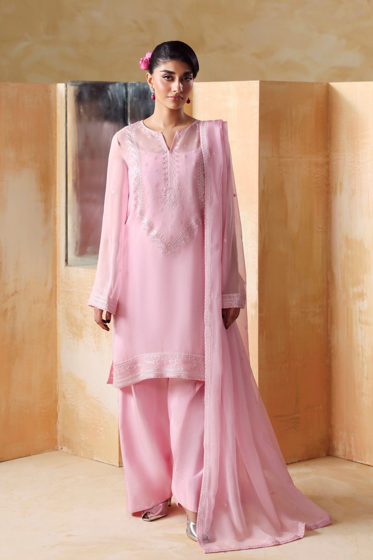 Woman in a pink traditional outfit standing against a beige wall with wooden panels.