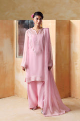 Woman in a pink traditional outfit standing against a beige wall with wooden panels.