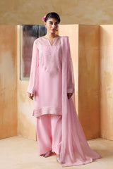 Woman in a pink traditional outfit standing against a beige wall with wooden panels.