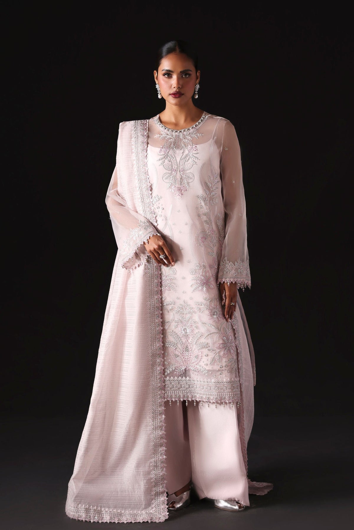Woman wearing a light pink traditional outfit with intricate patterns on a black background