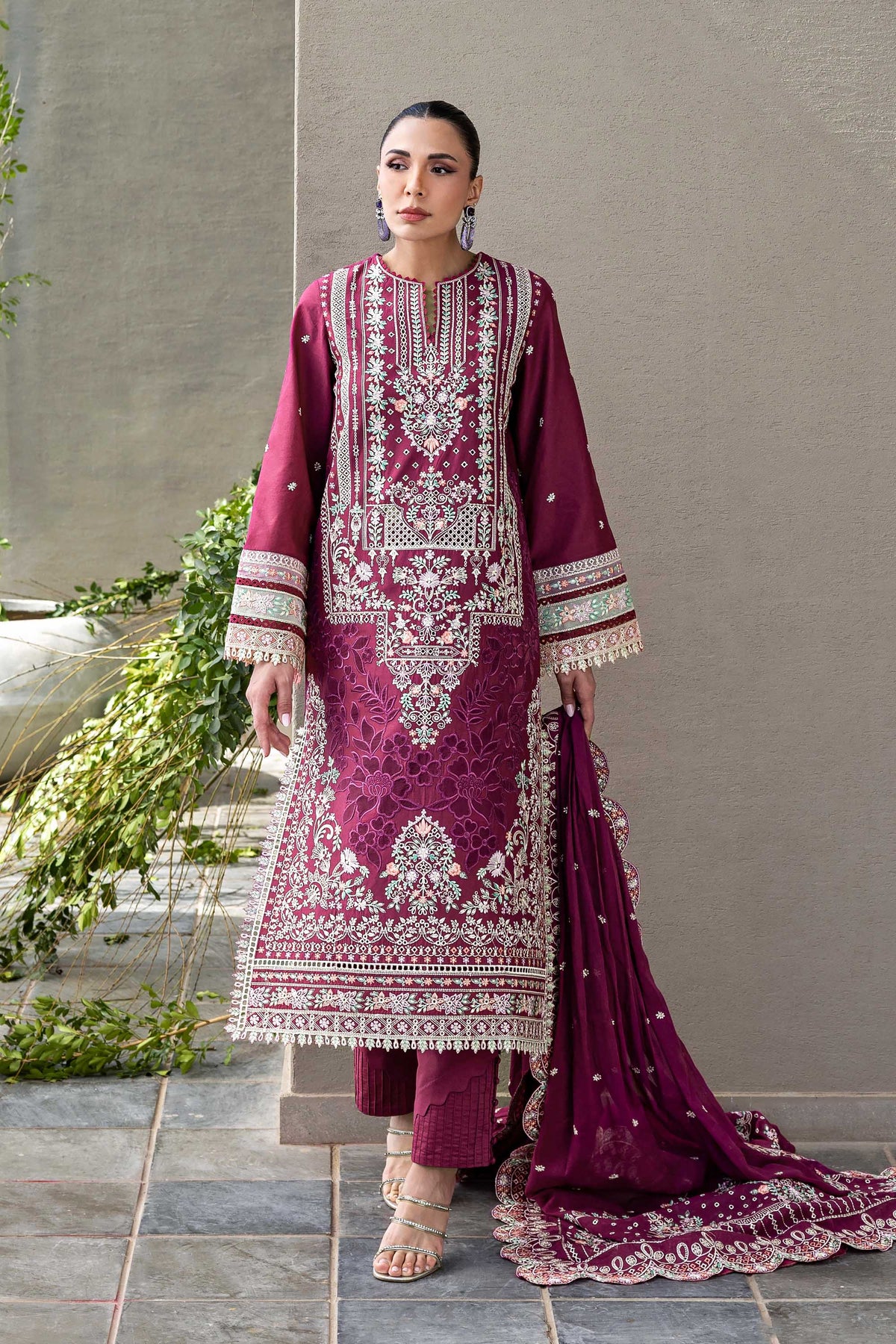 Woman wearing a traditional maroon embroidered outfit with a gray background