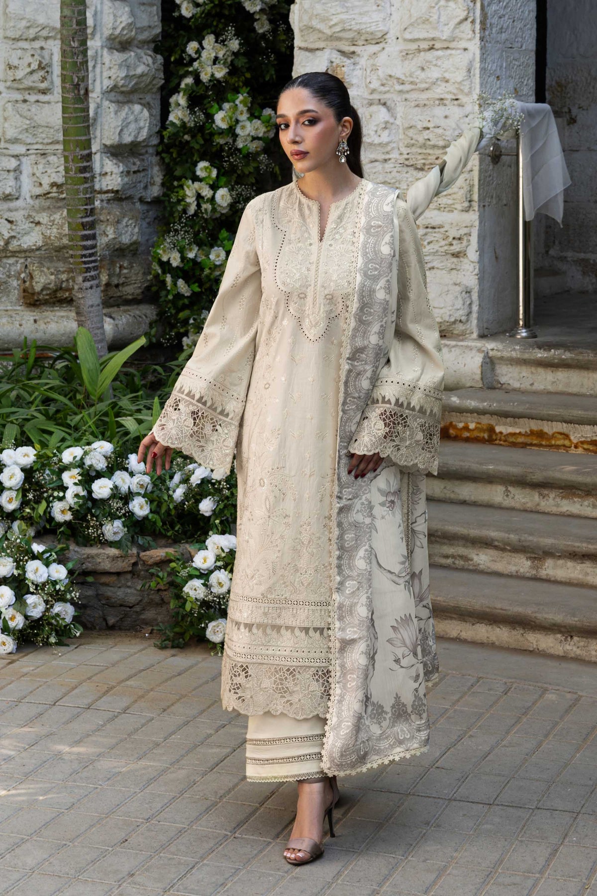 Woman in a traditional outfit standing outdoors with floral decorations.