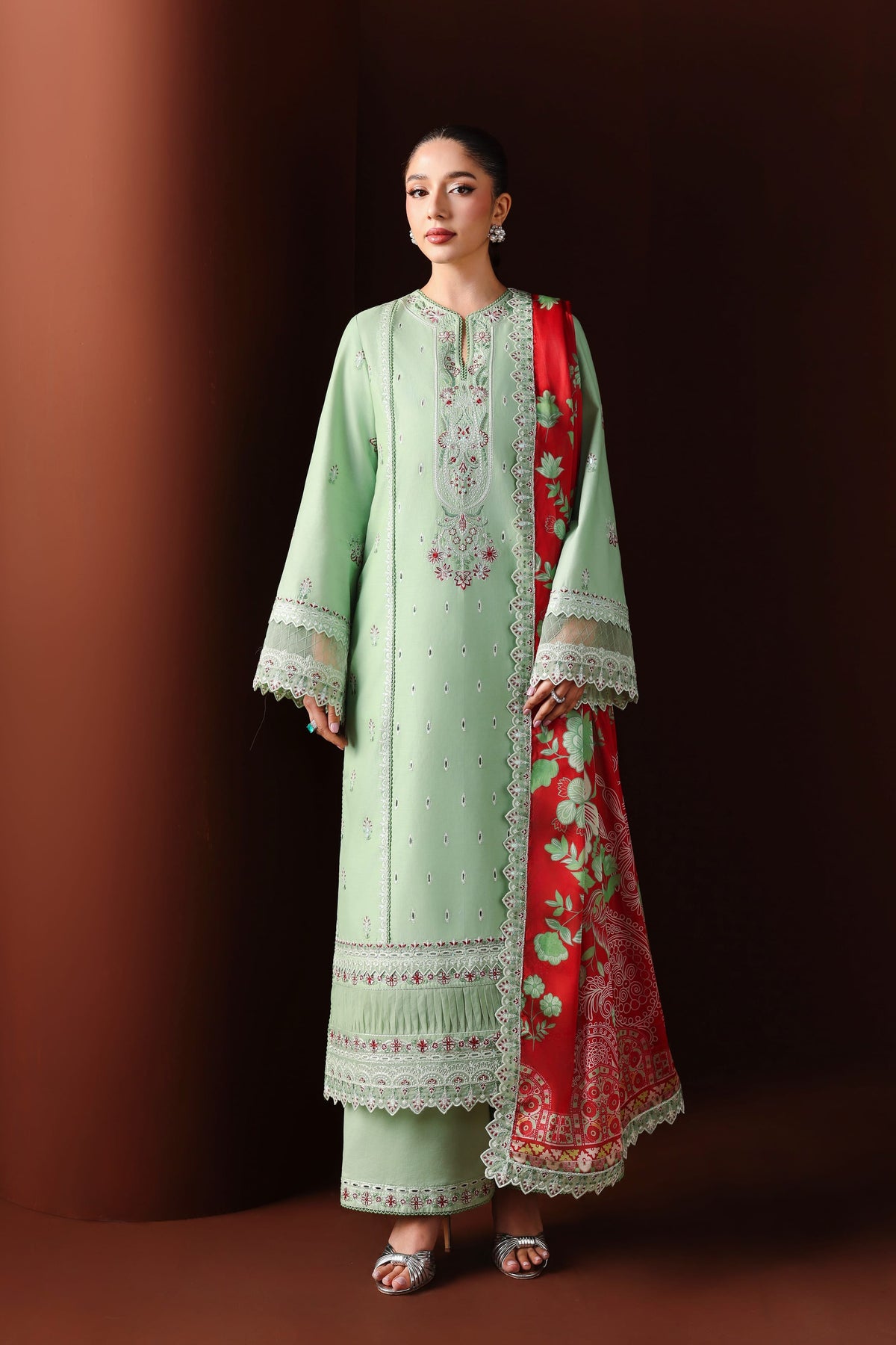 Woman wearing a light green embroidered outfit with a red dupatta against a dark background
