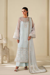 Woman wearing a light blue embroidered traditional outfit in a neutral setting