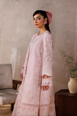 Woman in a pink traditional outfit standing against a textured wall with a plant and chair in the background.