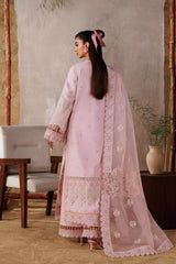Woman in a pink traditional outfit standing in a room with plants and furniture.