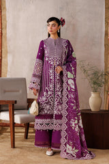 Woman in a purple embroidered outfit standing in a room with a white screen and decorative elements.