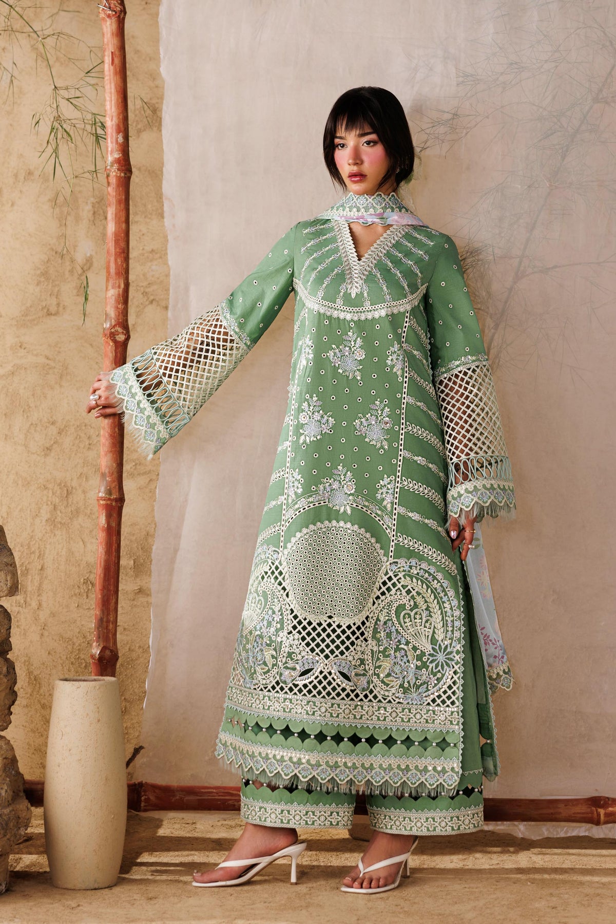 Woman in a green embroidered dress standing against a textured wall with decorative elements.