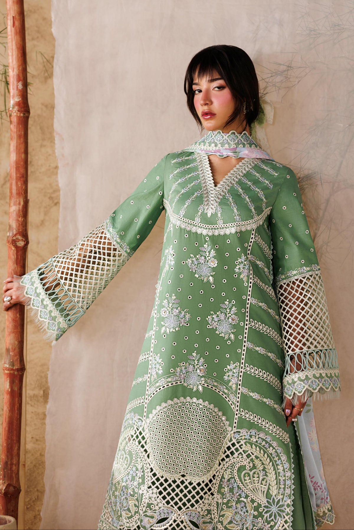 Woman wearing a green embroidered dress against a textured wall.