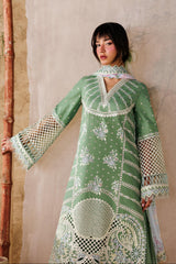 Woman wearing a green embroidered dress against a textured wall.