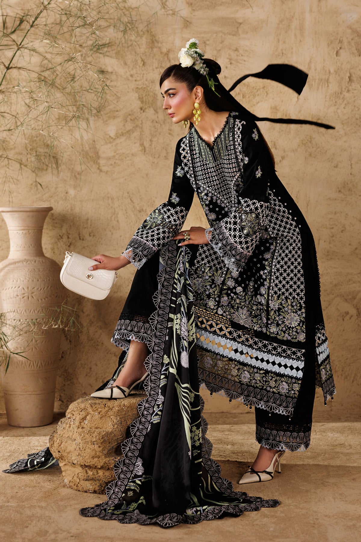 Woman in a black and white patterned dress standing against a beige wall with decorative vases.