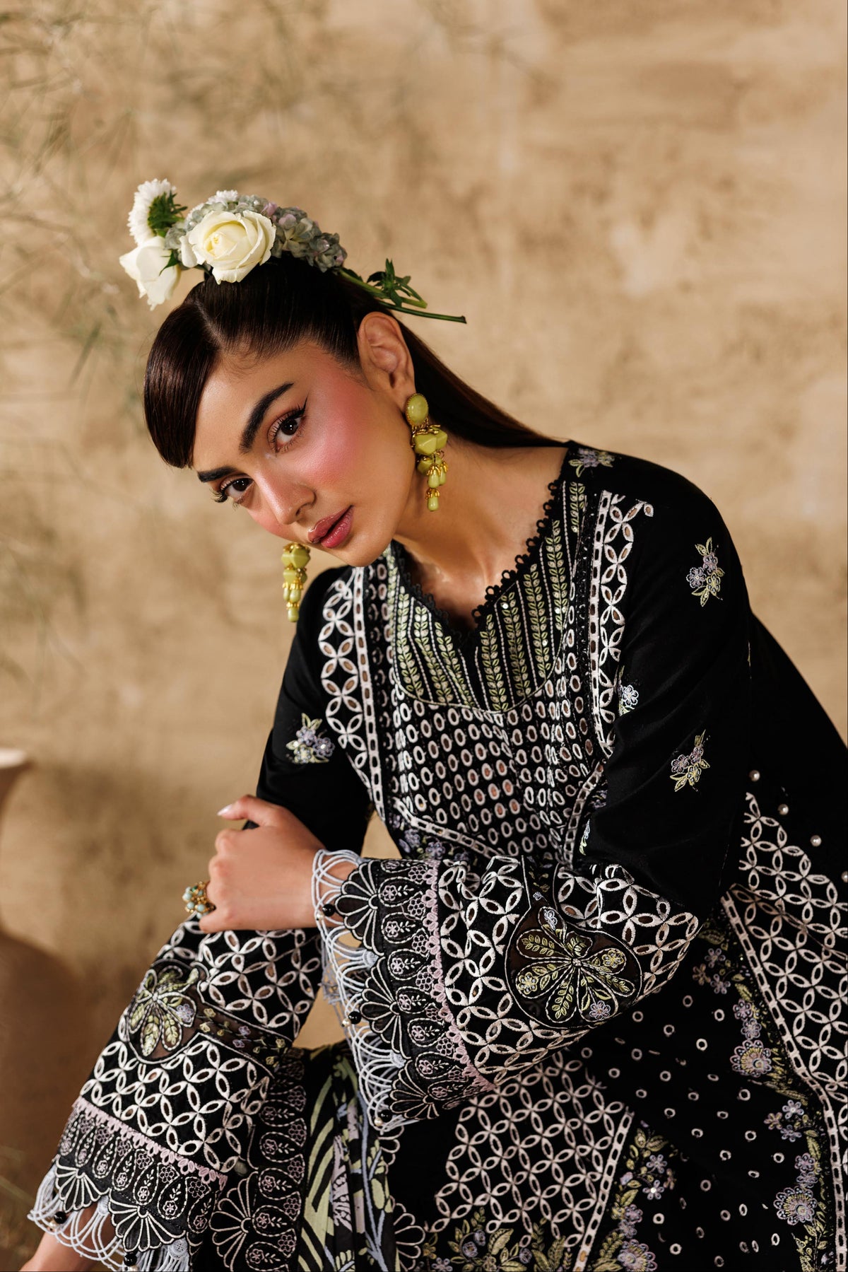 Woman in traditional embroidered outfit with floral headpiece against a beige wall.