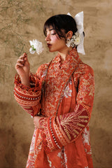 Woman in a traditional red and gold outfit holding a white flower against a beige wall.