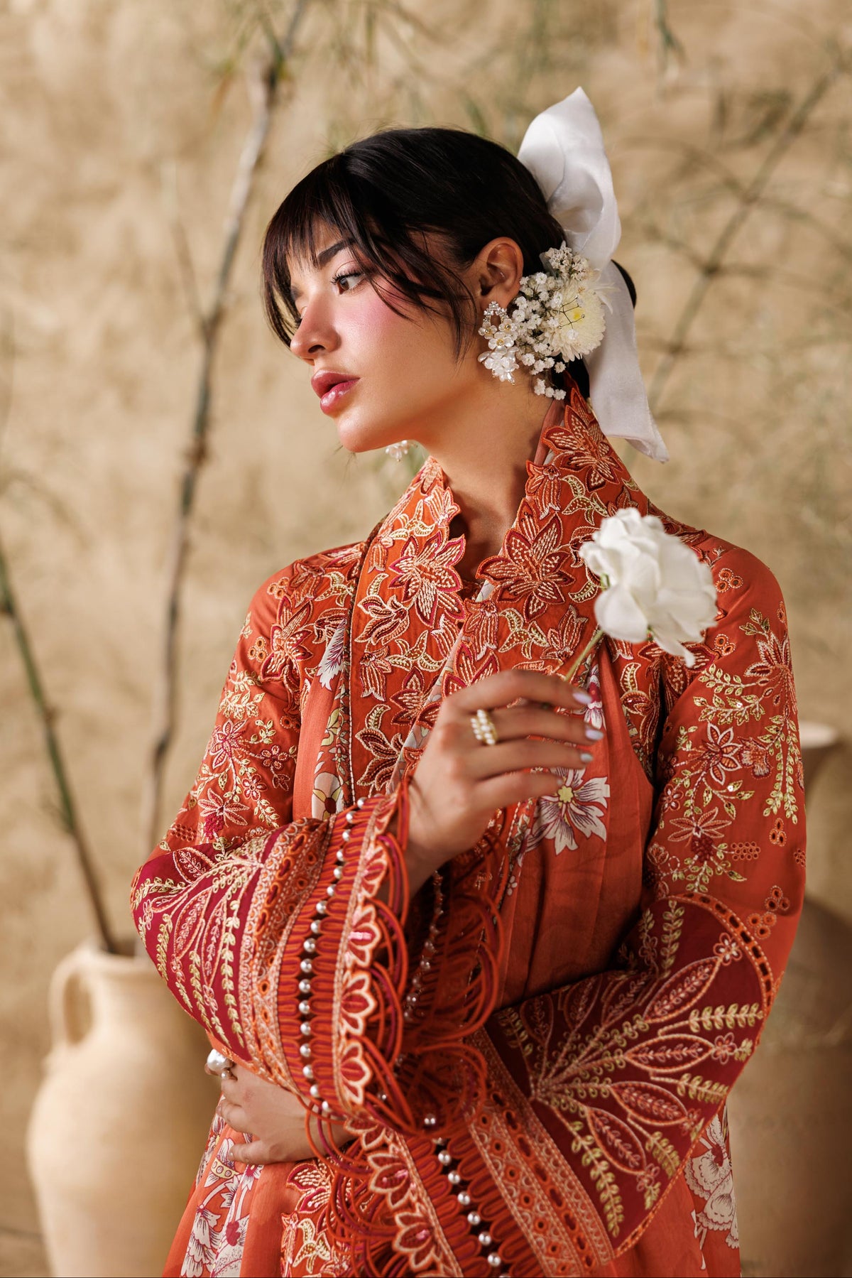 Woman in an orange embroidered outfit with floral hair accessories against a beige background