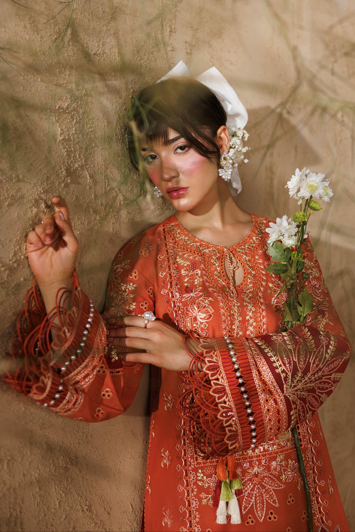 Woman in traditional attire holding flowers against a textured wall