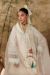 Woman in a white embroidered dress with a floral headpiece against a beige wall.