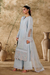 Woman in a light blue traditional outfit standing in a rustic setting with beige walls and decorative vases.