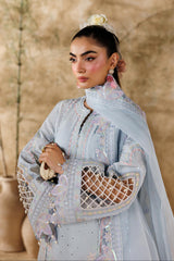 Woman in a light blue embroidered outfit with a textured beige wall background