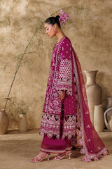 Woman in a traditional pink and purple outfit standing against a beige wall with decorative vases.