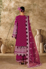 Woman in a traditional pink and white embroidered outfit standing against a beige wall with decorative vases.