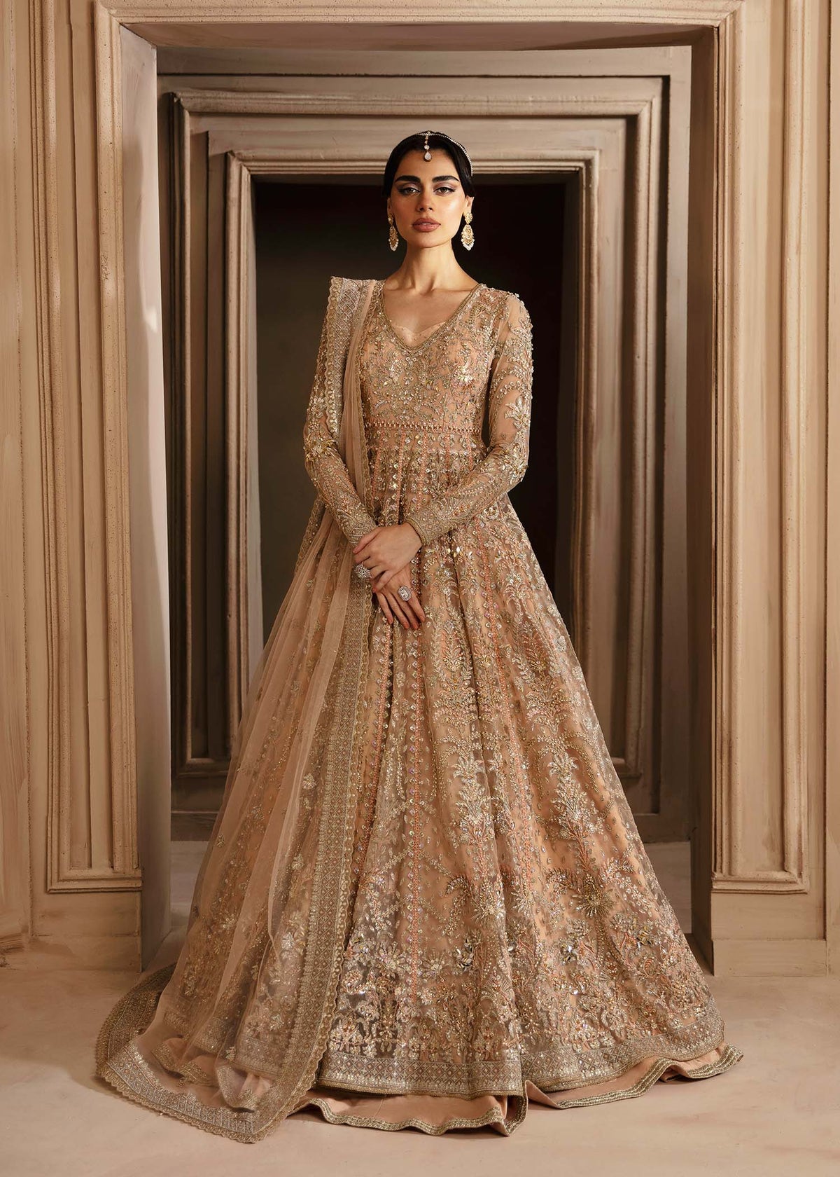 A woman wearing an elegant traditional dress with net embroidery and hand embellishments in gold and beige tones.