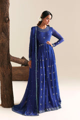 Woman in a blue traditional outfit standing against a neutral background with wooden logs.