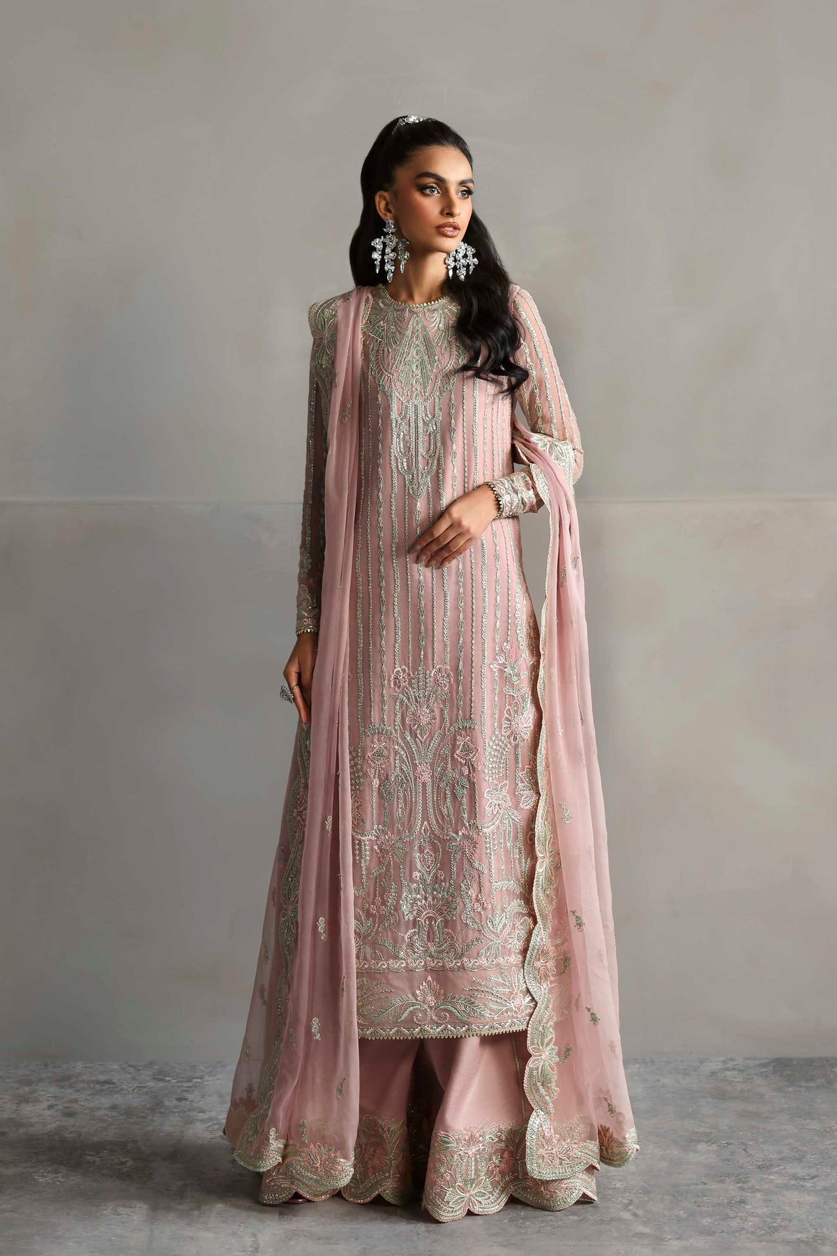 Woman wearing a pink embroidered traditional outfit with a matching dupatta against a plain background