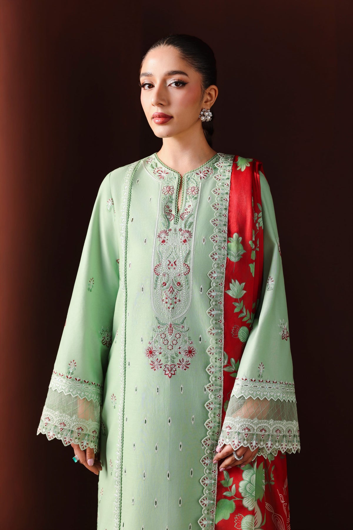 Woman wearing a light green embroidered outfit with a red dupatta against a dark background
