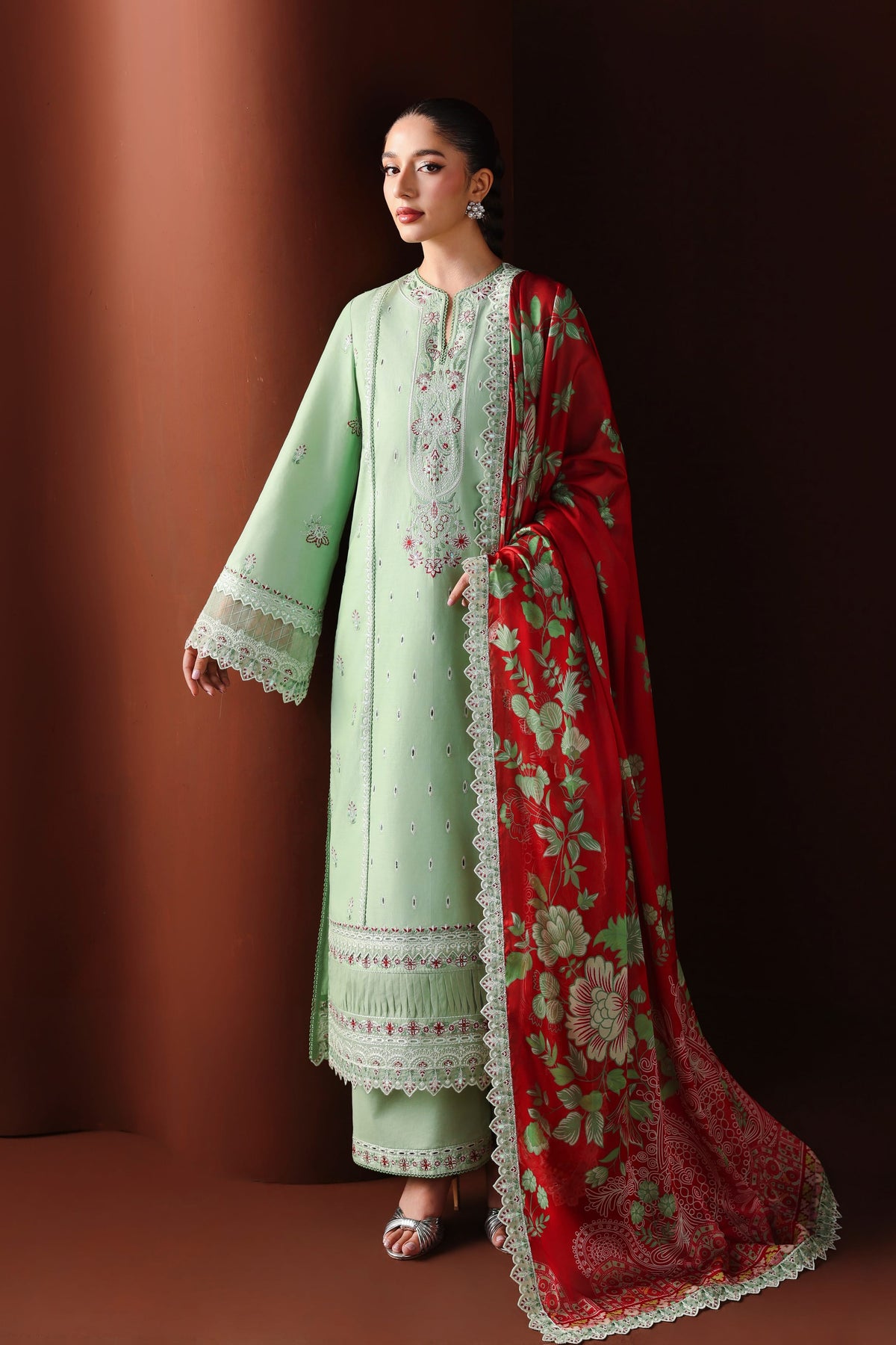 Woman wearing a light green embroidered outfit with a red dupatta against a brown background