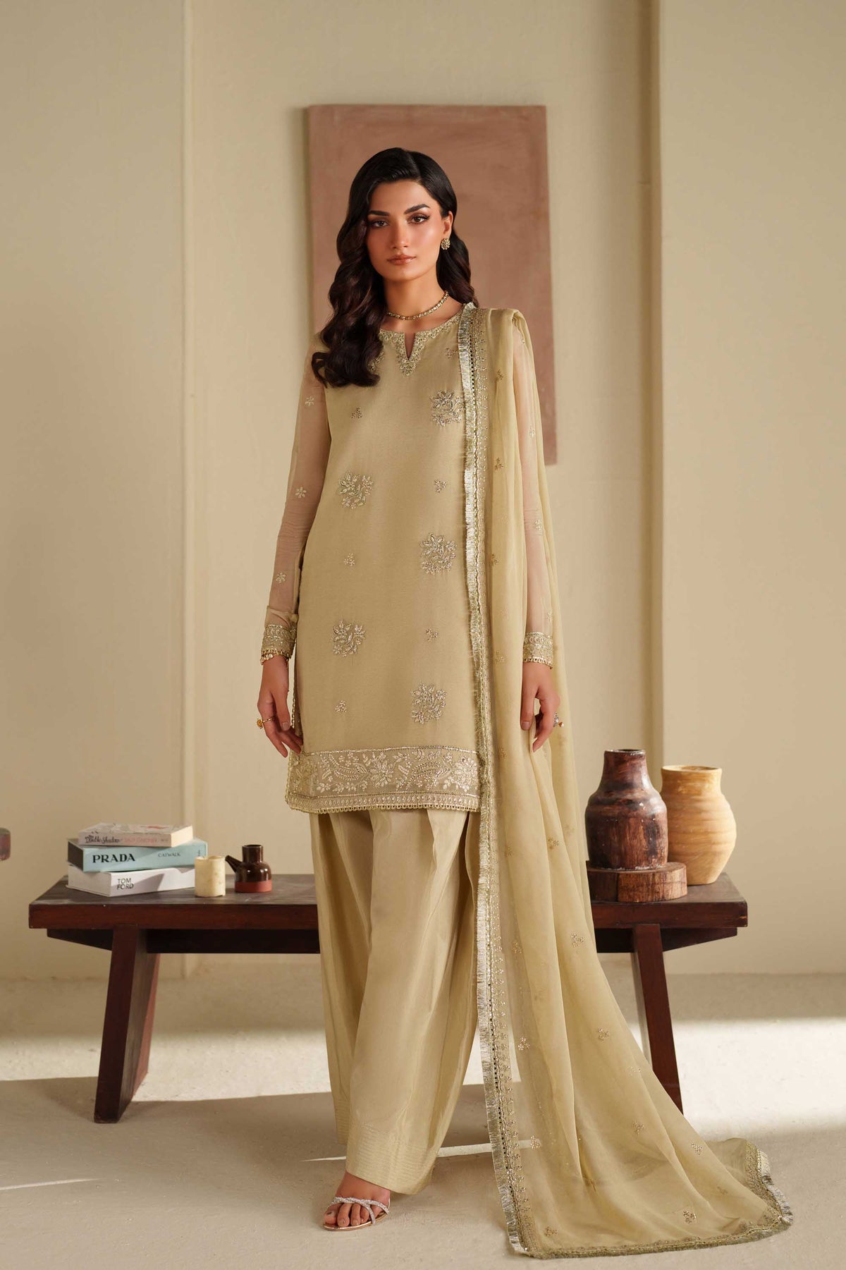Woman wearing a beige traditional outfit with a matching dupatta in a minimalistic room.