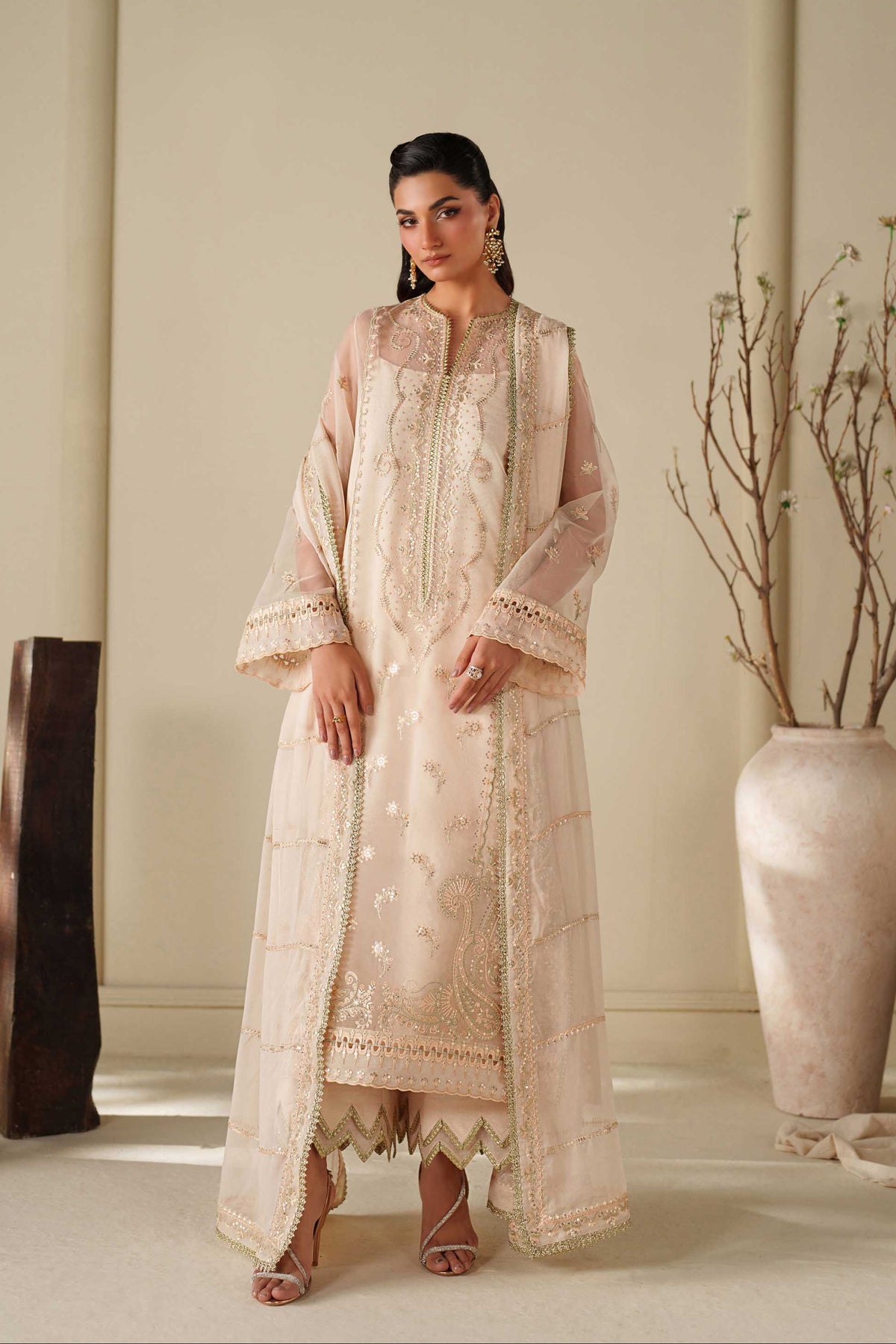 Woman in a traditional outfit standing in a minimalistic room with decorative elements.