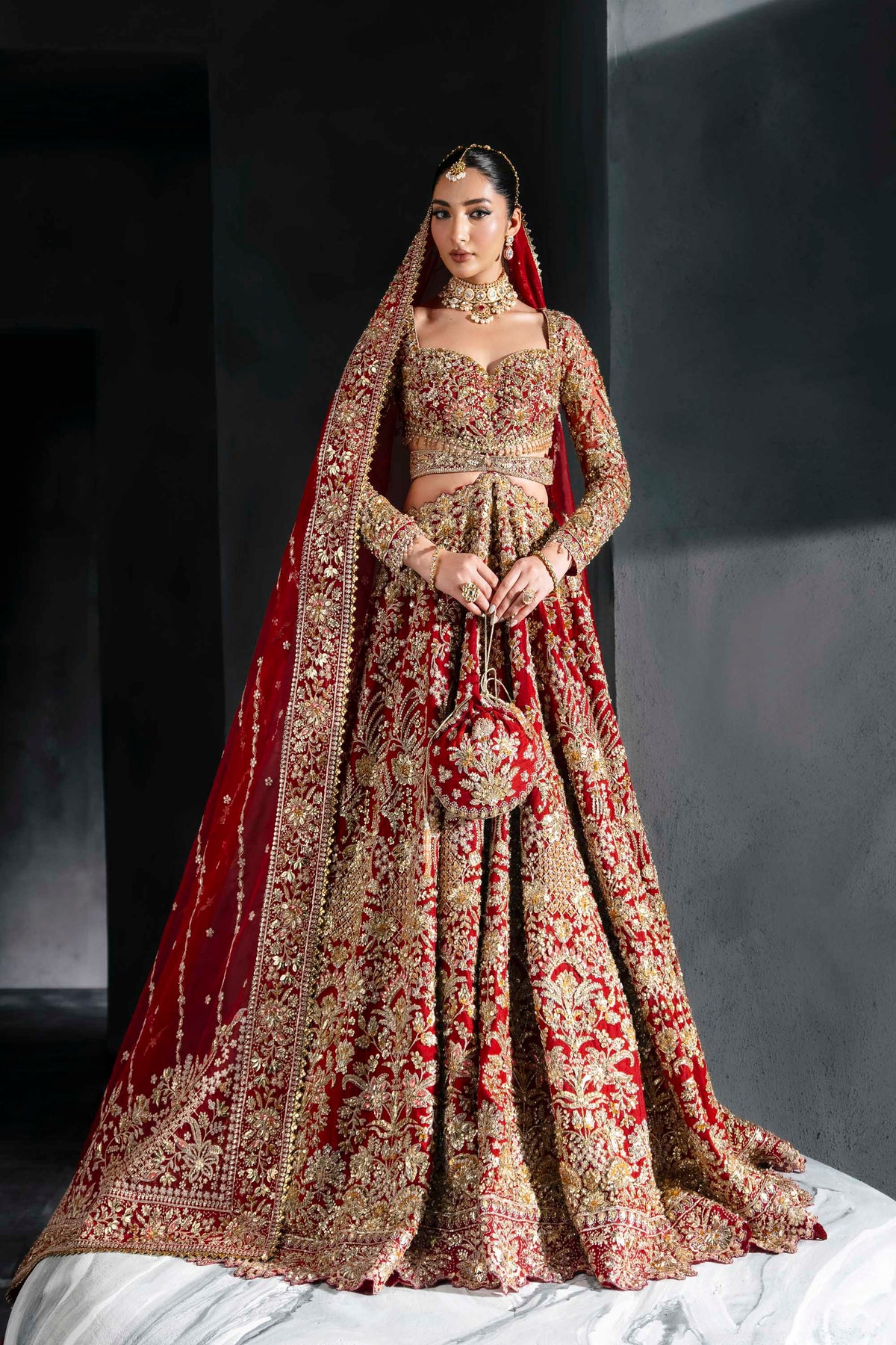 Woman in a traditional embroidered outfit with a red dupatta against a dark background